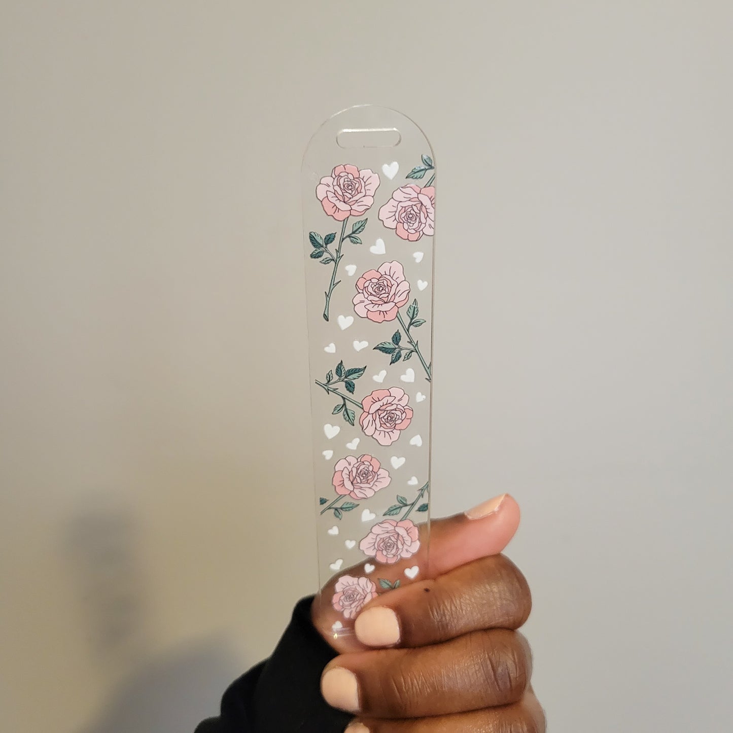 A person holding a double-sided UV DTF acrylic bookmark featuring pink roses and small hearts from SuppliedByKai, perfect for floral-themed reading accessories.
