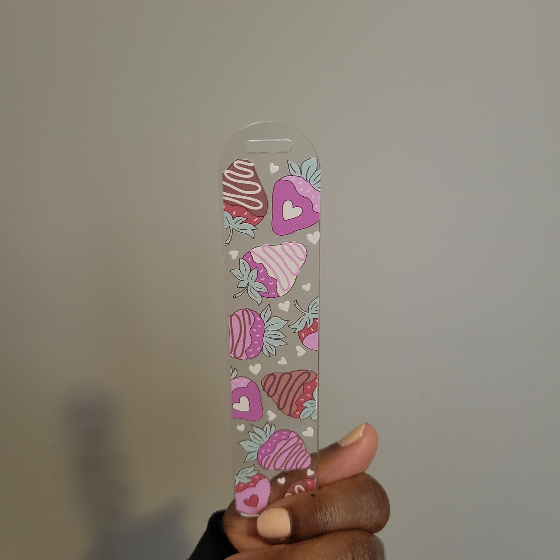 A hand holding an UV DTF double-sided acrylic bookmark decorated with chocolate-dipped strawberries and pink hearts from SuppliedByKai